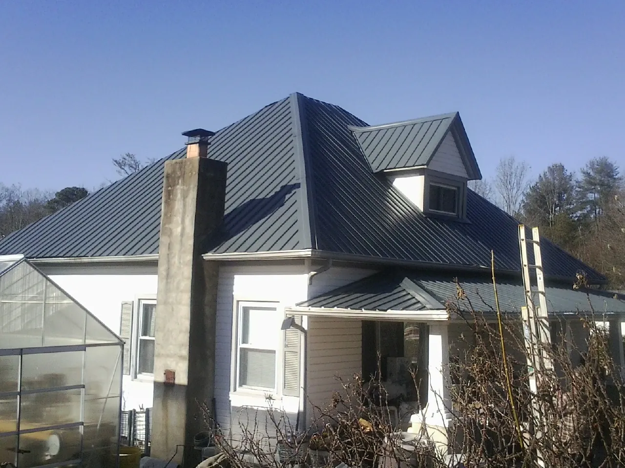 Dark blue standing seam metal roof on a white farmhouse with dormer — Slate & Tile Roof Repair by Roofing Brothers in Flint Hill