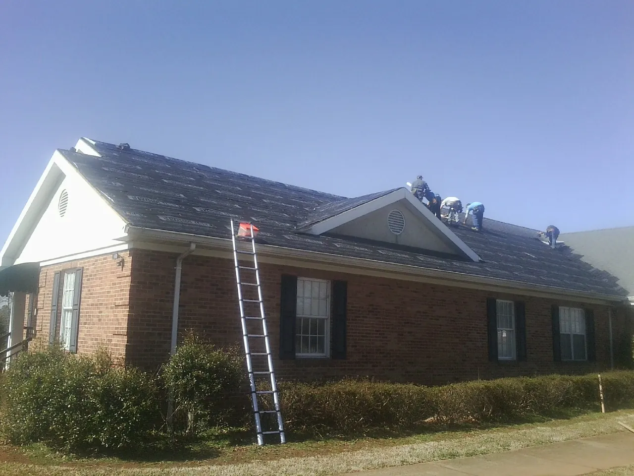 Crew tearing shingles off a brick ranch roof with a ladder set — Metal Roof Repair work by our crew in Flint Hill