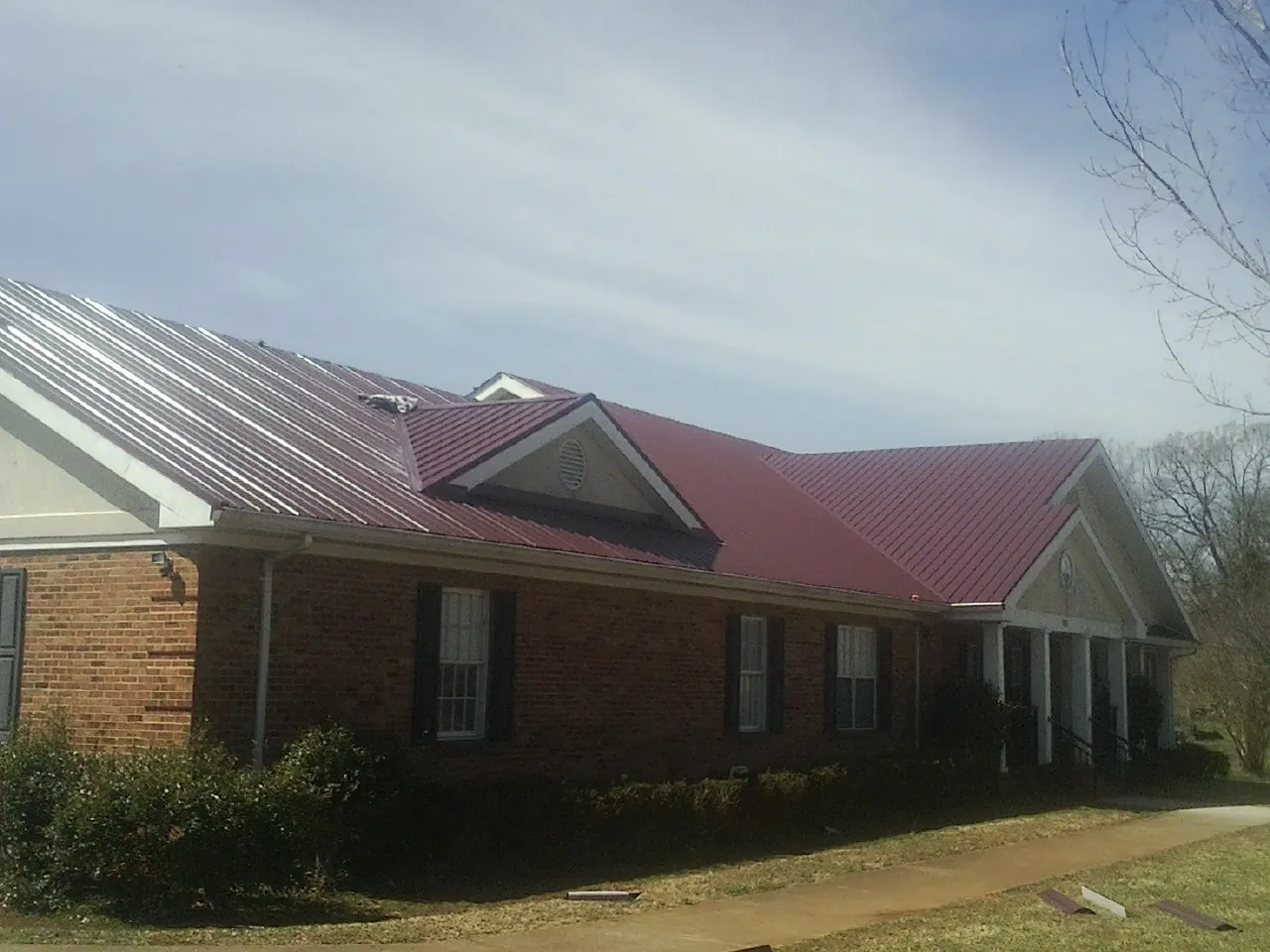 Red metal roof with gabled entries on a long brick building, from a Hail Damage Roof Repair job in Flint Hill