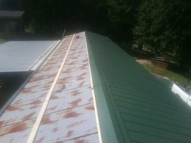 Old rusted panels beside newly installed green metal roofing — Wind Damage Roof Repair by Roofing Brothers in Flint Hill