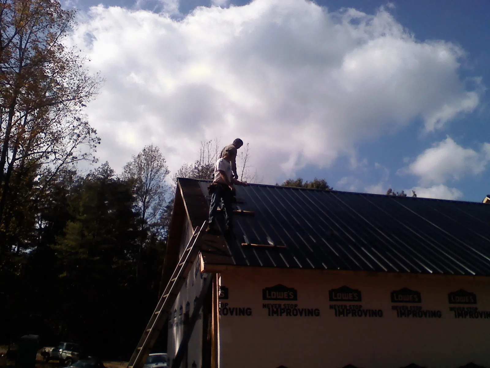 Roofer fastening dark metal panels high against a cloudy sky, from a Roof Inspection job in Flint Hill