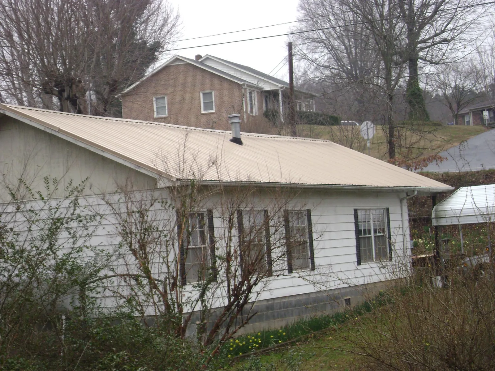 Tan metal roof on a white sided house set into a hillside — Commercial Roofing by Roofing Brothers in Flint Hill