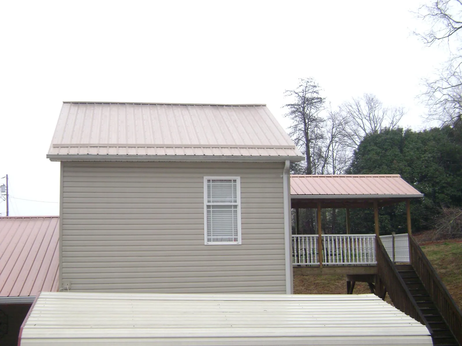 Tan metal roofs on a two story addition and attached porch, from a Roof Replacement job in Flint Hill